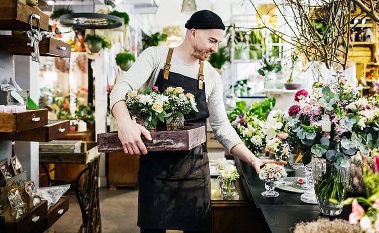 Junger Mann mit Mütze arbeite in einem Blumenladen.