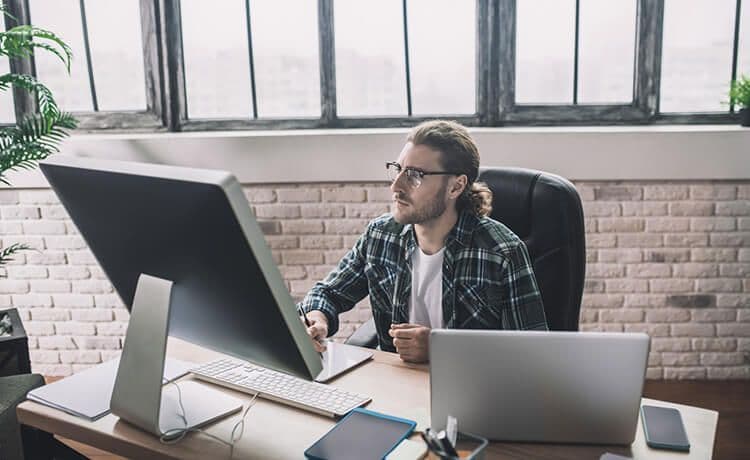 Informatiker mit Brille und Hemd sitzt an einem PC im Büro.