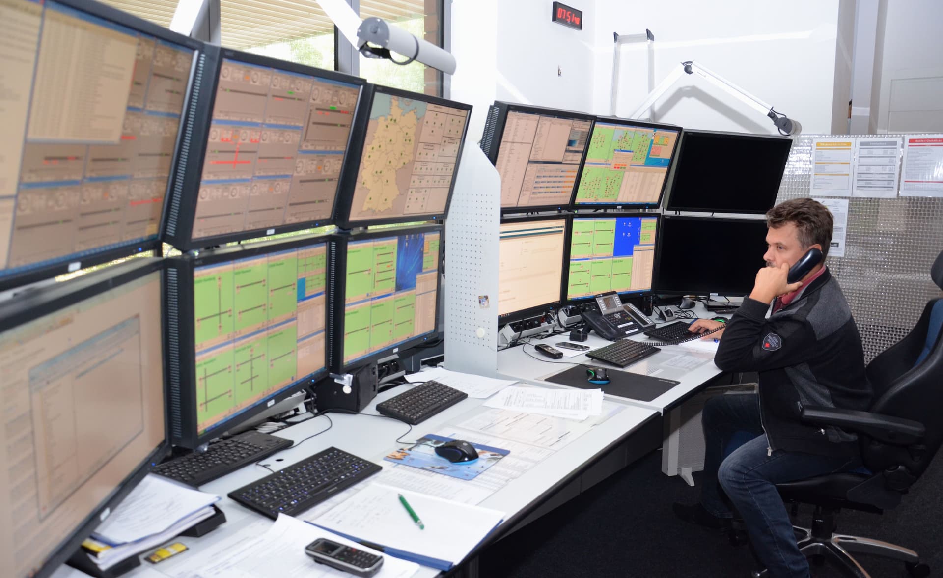 Ein Mann sitzt vor einer Wand von Monitoren und telefoniert.