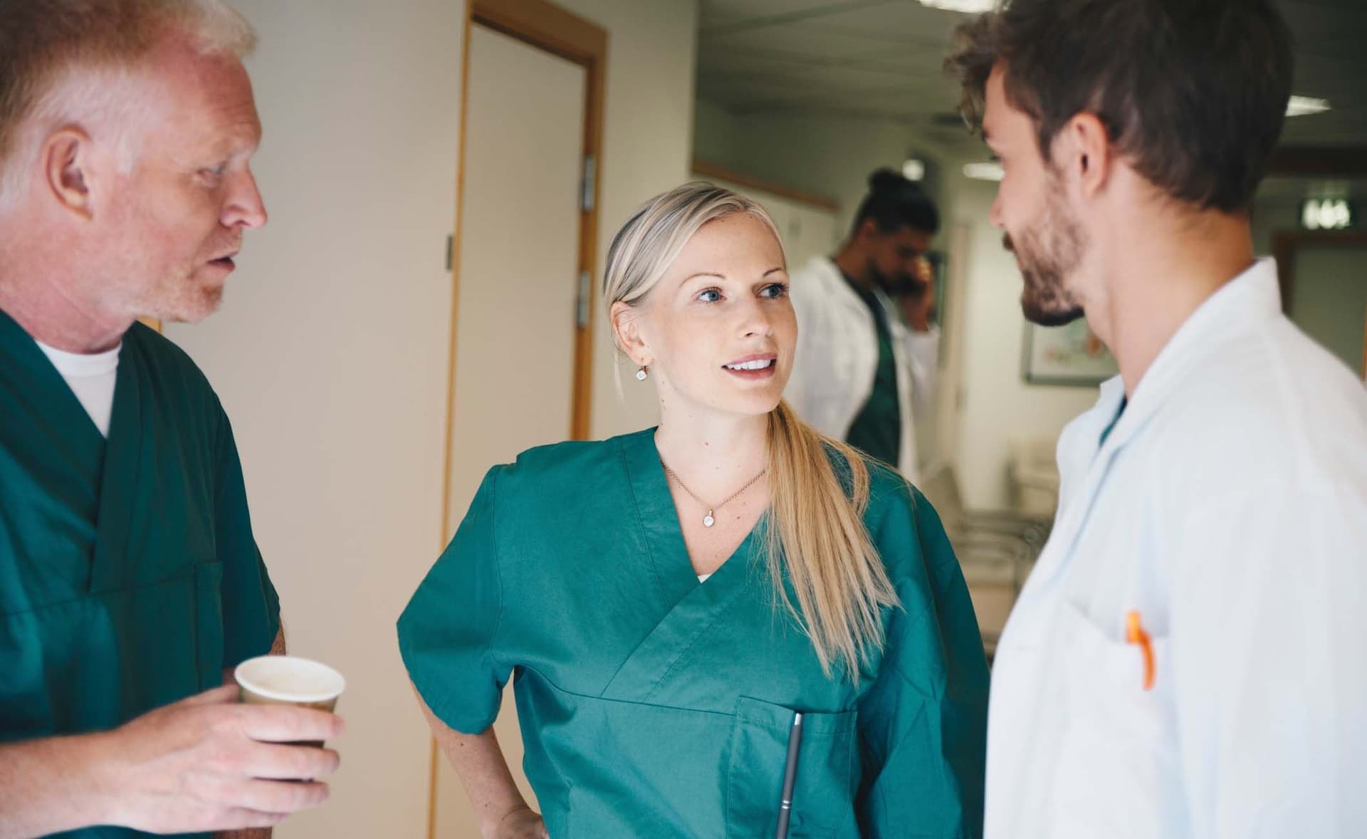 Zwei Krankenpfleger und ein Arzt stehen im Krankenhausflur und unterhalten sich