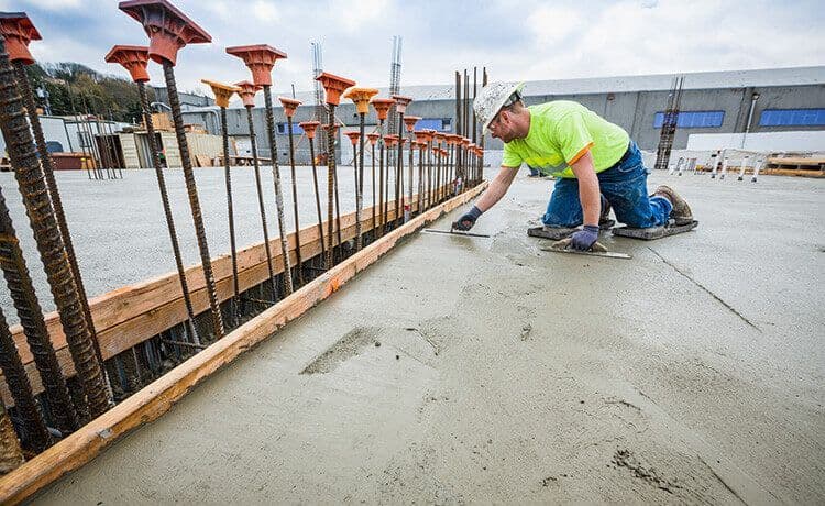 Beton- und Stahlbetonbauer zieht auf einer Baustelle den Beton glatt.