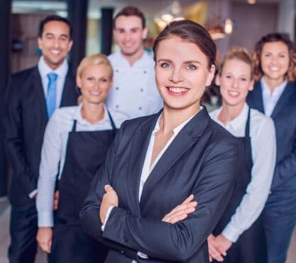 Frau im Anzug und eine Gruppe Menschen gucken in die Kamera.