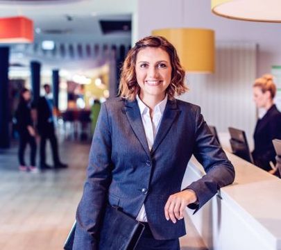 Junge Frau im Anzug steht an einer Rezeption.