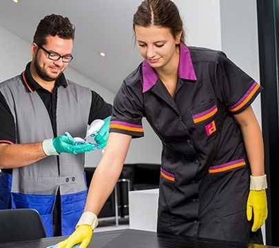 Eine Frau und ein Mann in Putzkitteln, die Tische säubern