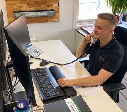 Azubi sitzt am Schreibtisch vorm PC und telefoniert.