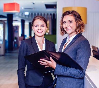 Zwei Frauen im Anzug stehen in einer Hotellobby.