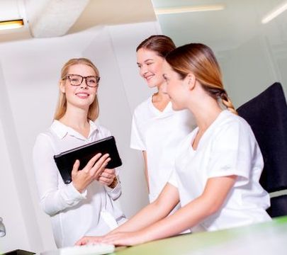 Drei Studentinnen in Arztkleidung lächeln in die Kamera.