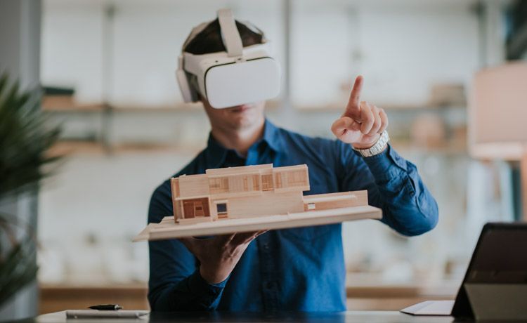 Junger Mann mit VR-Brille hält das Modell eines Gebäudes in den Händen. Junger Mann mit VR-Brille hält das Modell eines Gebäudes in den Händen.
