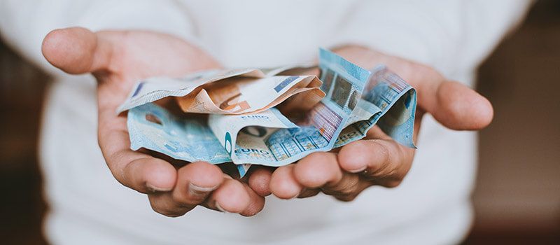 Junger Mensch hält mehrere Euro-Scheine in den offenen Händen