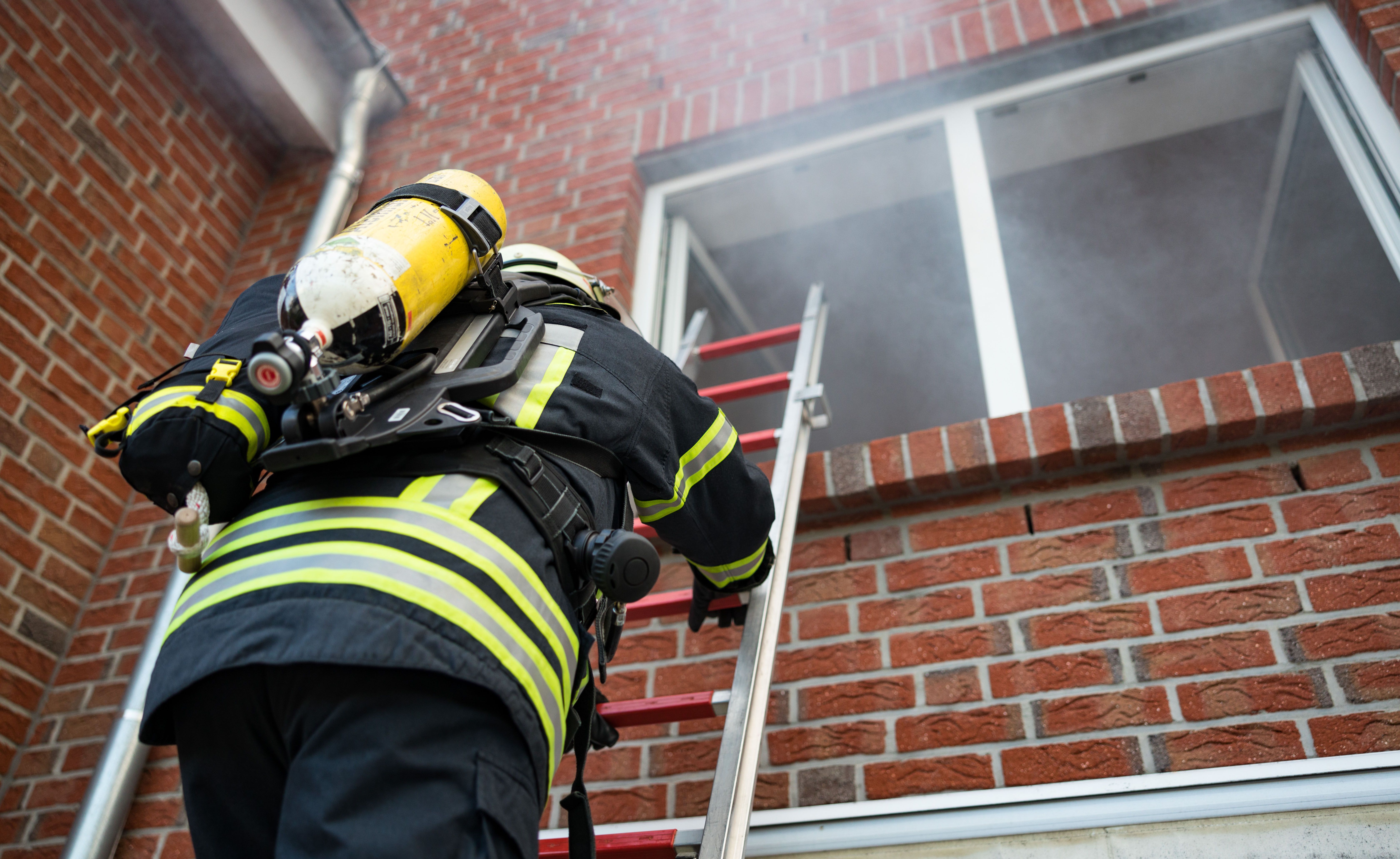 Feuerwehrmann klettert in ein Fenster aus dem Rauch raus kommt.