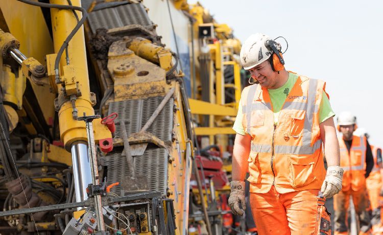 Mann in Arbeitskleidung steht auf einer Baustelle neben einer Maschine.
