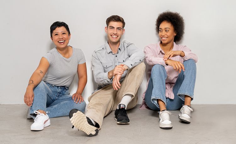 Drei Menschen sitzen vor einer weißen Wand und lächeln in die Kamera. Drei Menschen sitzen vor einer weißen Wand und lächeln in die Kamera.