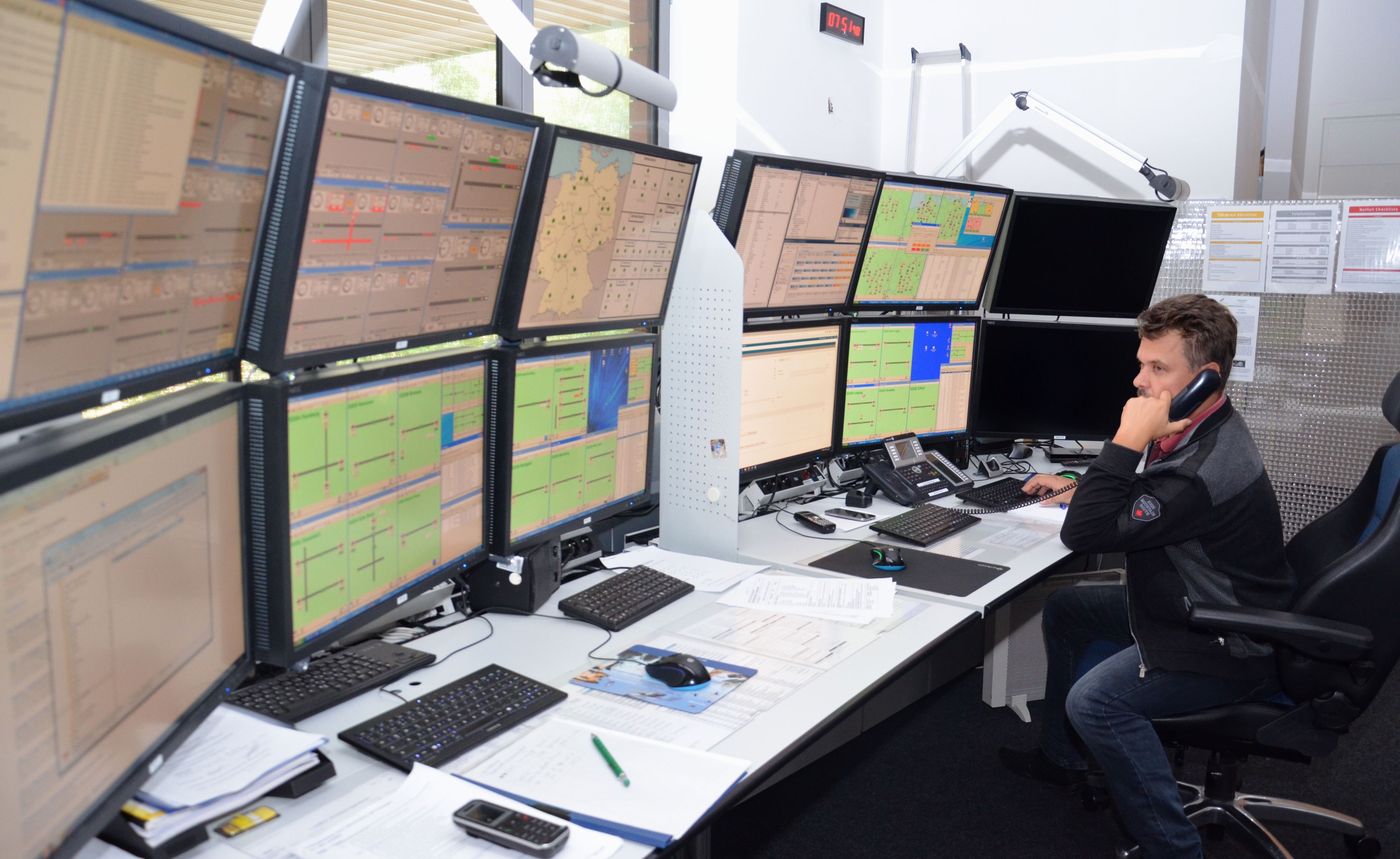 Ein Mann sitzt vor einer Wand von Monitoren und telefoniert.
