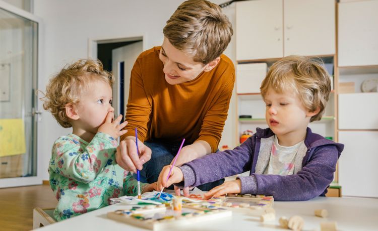 Junge Sozialarbeiterin spricht mit Kindern, die malen. Junge Sozialarbeiterin spricht mit Kindern, die malen.
