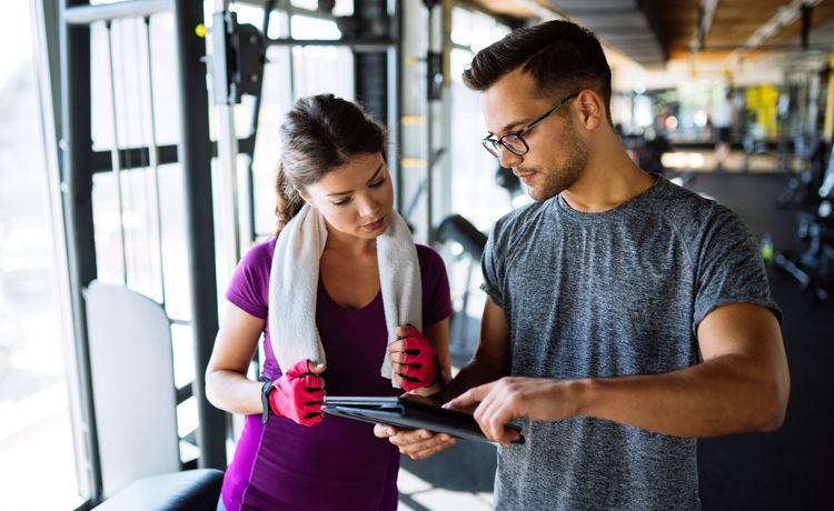 Mann und Frau stehen in einem Fitnessstudio und gucken auf ein Tablet.