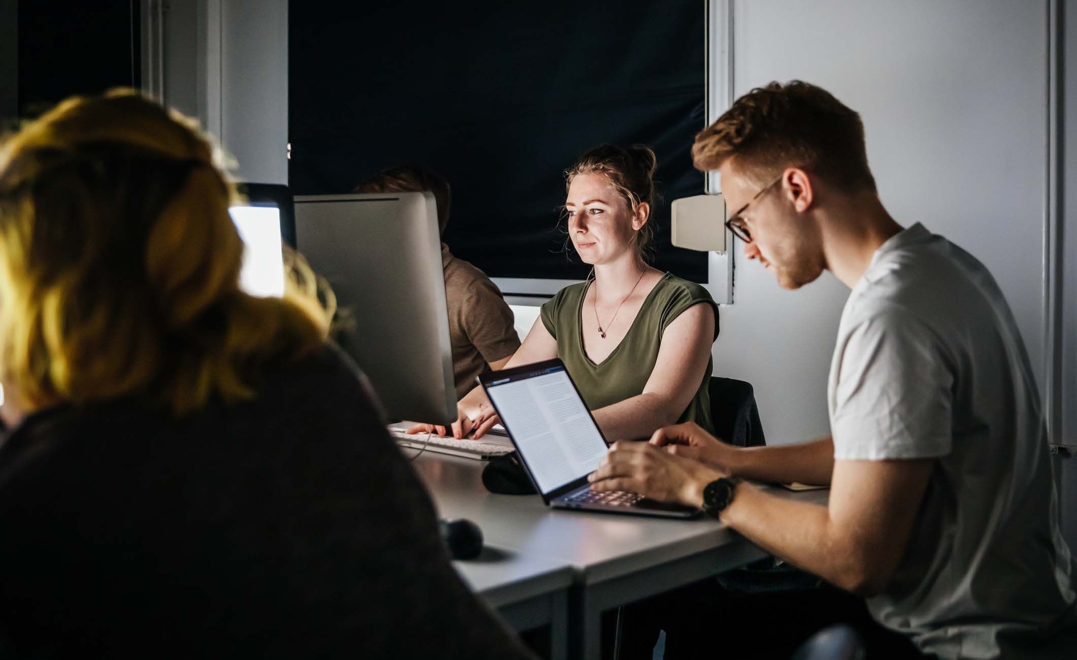 Studierende sitzen in einem dunklen Raum am PC.