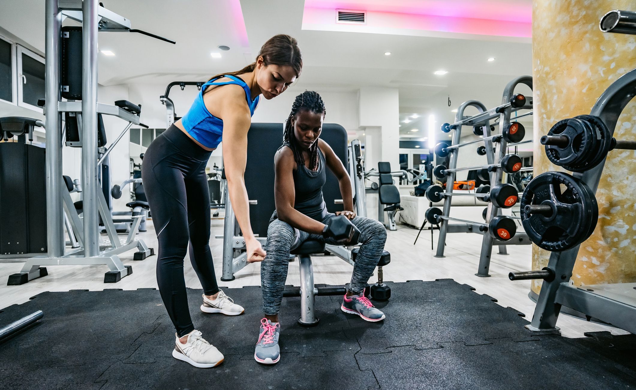 Fitnesstrainerin hilft Kundin bei einer Übung.