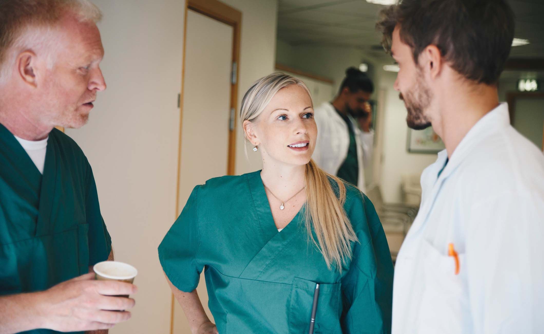 Zwei Krankenpfleger und ein Arzt stehen im Krankenhausflur und unterhalten sich