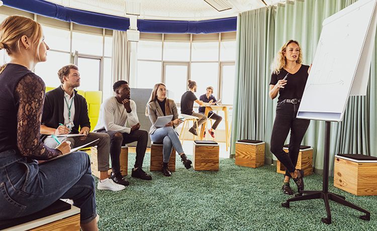 Studenten sitzen in einem Raum und gucken auf ein Flipchart.