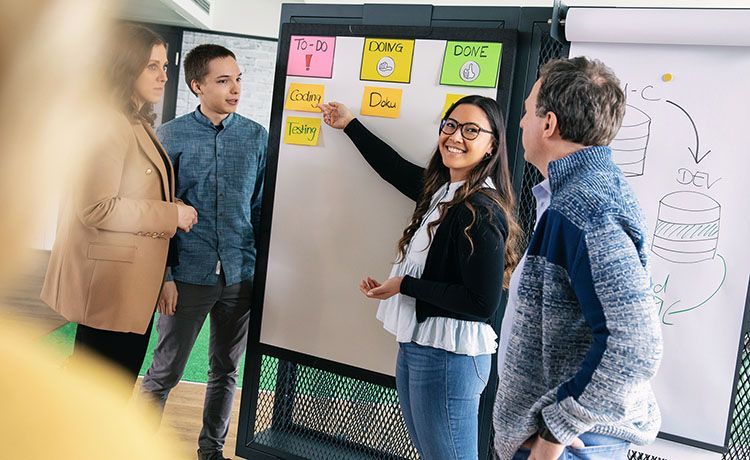 Mehrere Menschen schauen auf ein Flipchart mit bunten Zetteln, eine Frau zeigt auf einen Zettel. Mehrere Menschen schauen auf ein Flipchart mit bunten Zetteln, eine Frau zeigt auf einen Zettel.