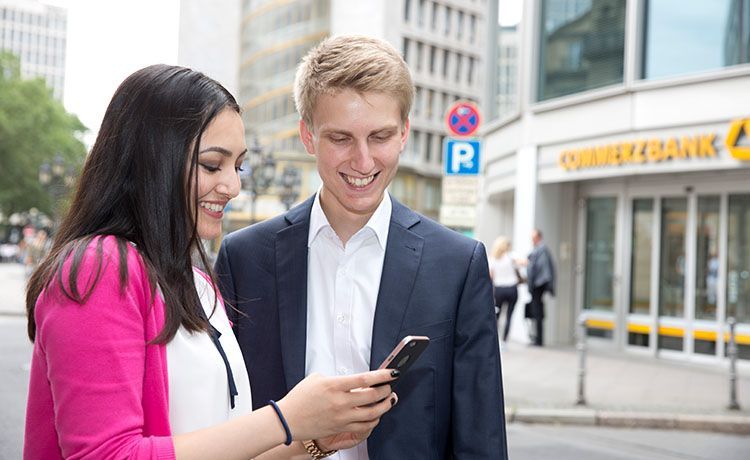 eine Frau und ein Mann stehen vor der Commerzbank und schauen auf ein Handy. eine Frau und ein Mann stehen vor der Commerzbank und schauen auf ein Handy.
