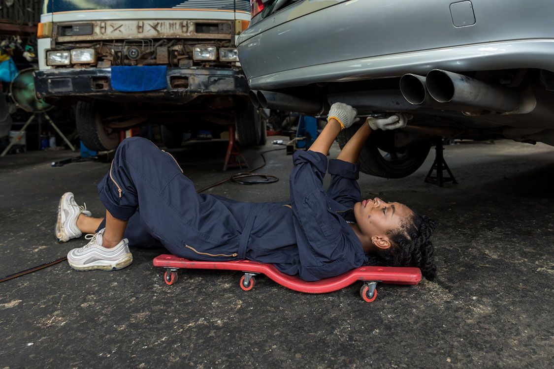 Karosserie- und Fahrzeugbaumechanikerin bei der Arbeit unterm Auto.
