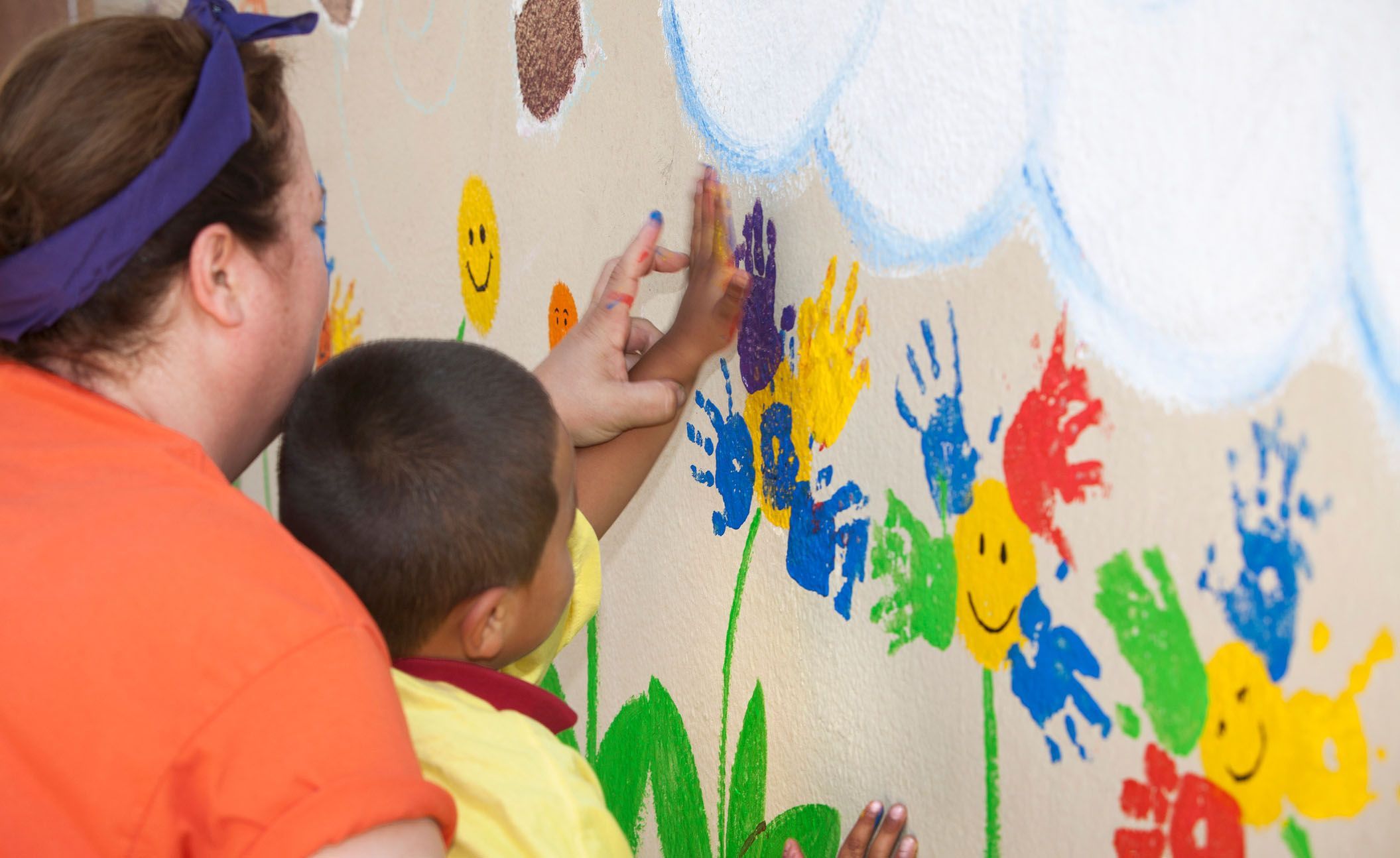 Kinderpflegerin bemalt eine Wand mit einem Kind.