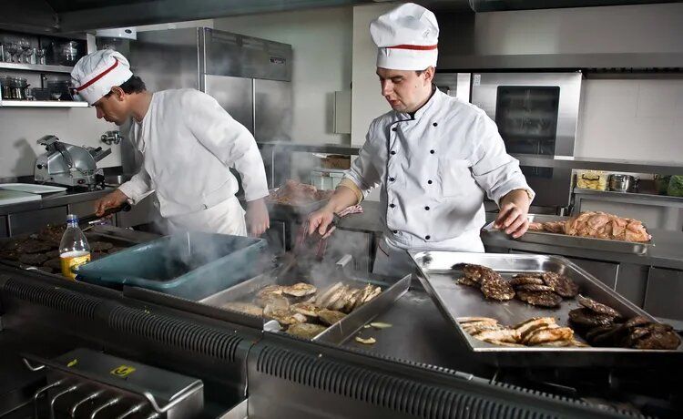 Zwei Köche bereiten in der Restaurantküche Fleischgerichte zu.