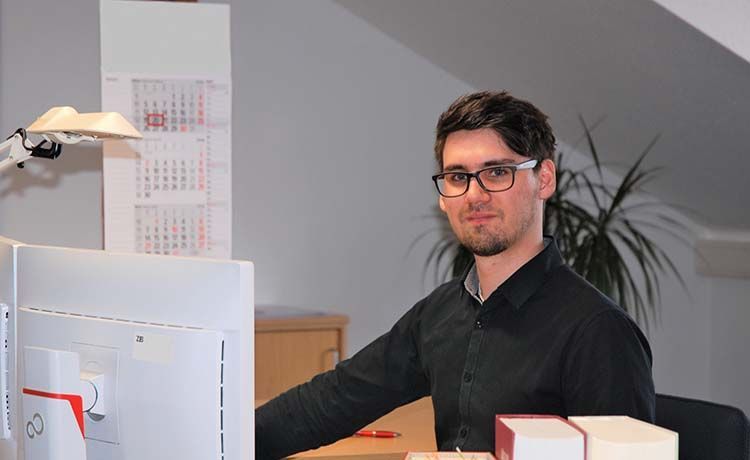 Junger Mann sitzt im Büro am Schreibtisch. 