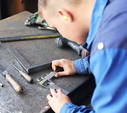 Ein Azubi misst ein Stück Metall ab.