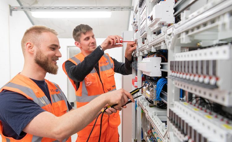 Zwei Azubis arbeiten an einem Stromkasten.