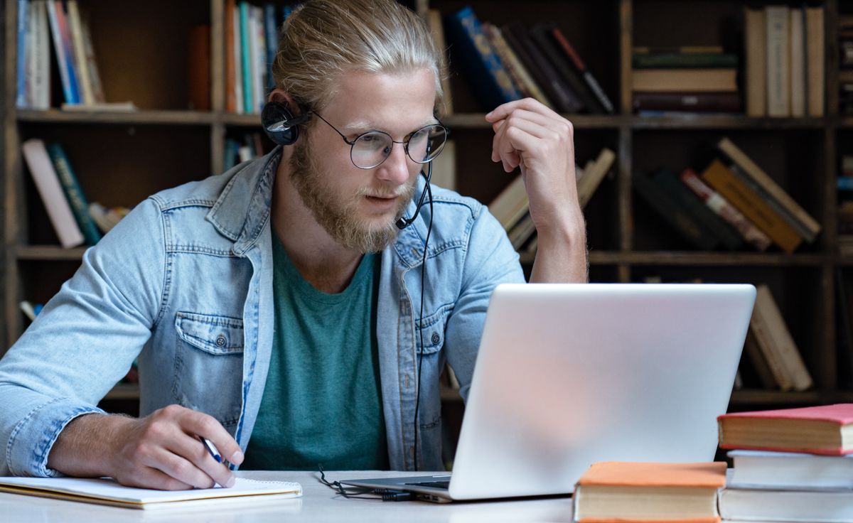 Übersetzer sitzt mit Headset am Schreibtisch und übersetzt einen Text am Laptop.