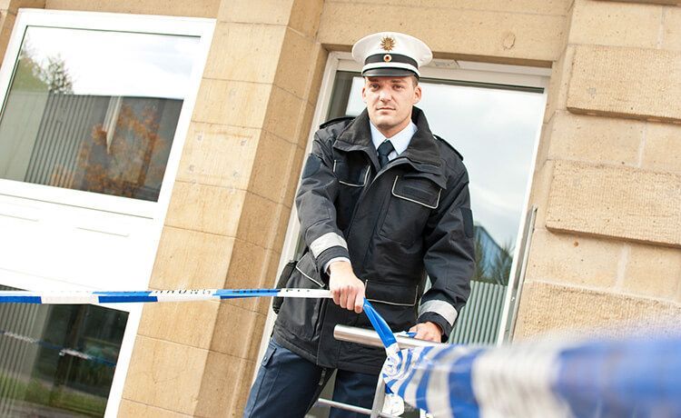 Junger Polizist sperrt Straße mit blau-weißem Flatterband ab.