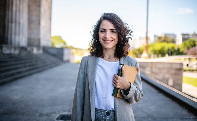 Junge Frau steht mit einem Buch in der Hand vor Gerichtsgebäude.