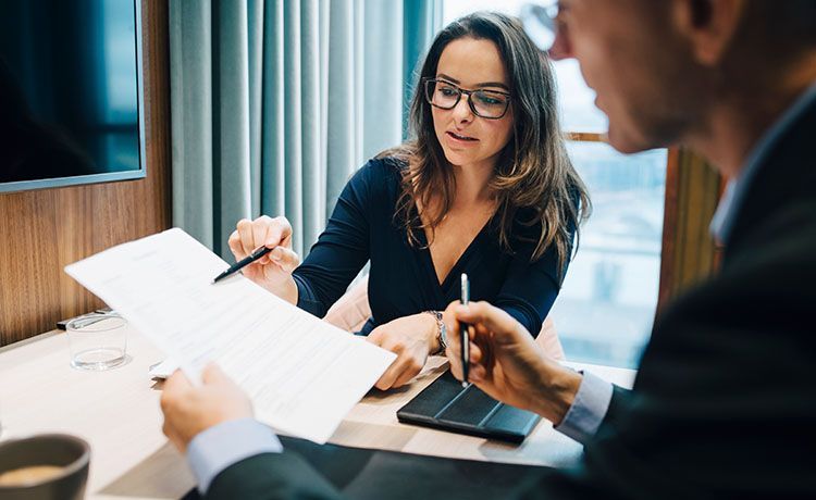 Frau zeigt mit einem Stift auf Dokumente.