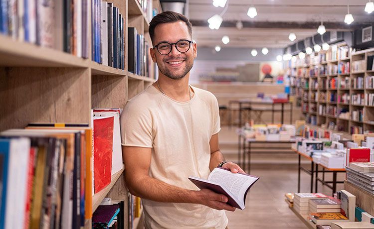 Junger Mann steht mit einem Buch in einer Buchhandlung.