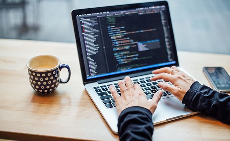 Junge Frau arbeitet an einem Laptop am Schreibtisch und schreibt Quellcode.