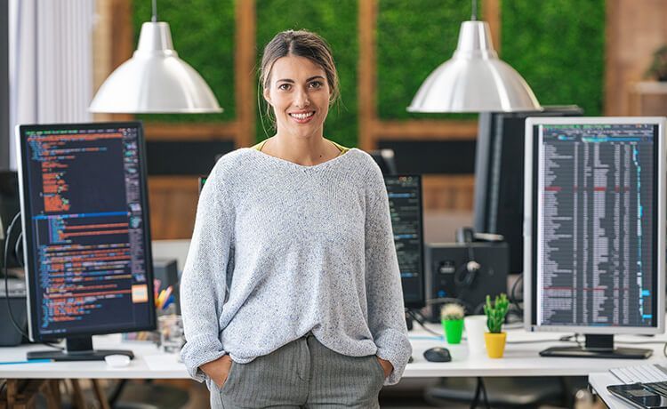 Junge Programmiererin steht in einem Büro vor Computern mit Code und schaut in die Kamera. Junge Programmiererin steht in einem Büro vor Computern mit Code und schaut in die Kamera.