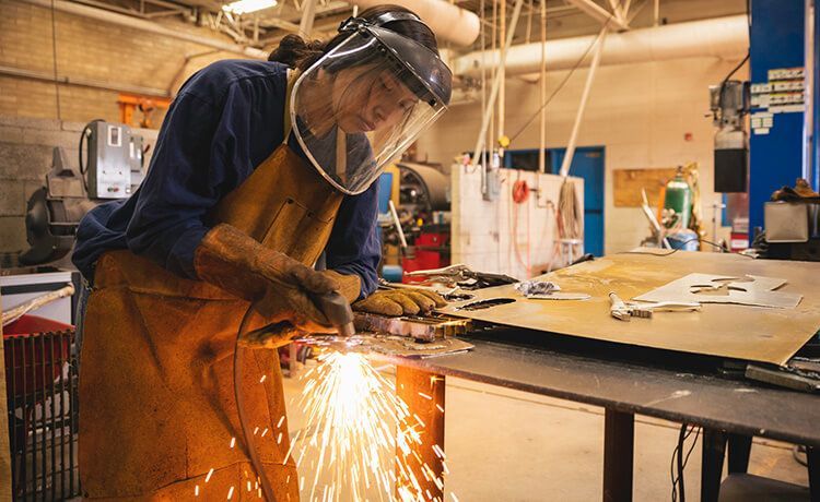 Schweißer steht in der Werkstatt und bearbeitet ein Metallteil bei dem viele Funken entstehen.