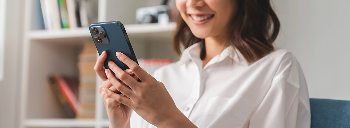 Social Media Managerin blickt lächelnd auf ein Smartphone, das sie in den Händen hält.
