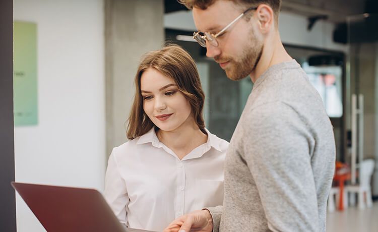 Zwei junge Verwaltungsfachangestellte in Ausbildung schauen auf Laptop und besprechen Aufgaben.