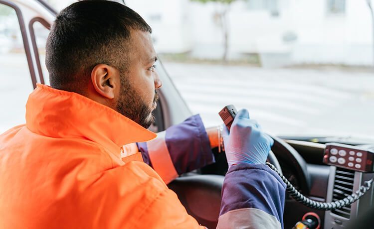 Junger Rettungssanitäter sitzt in einem Krankenwagen und hält Funkgerät in der Hand.