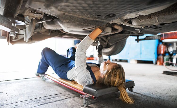 Kfz-Mechatronikerin liegt unter einem Auto und führt eine Reparatur durch.
