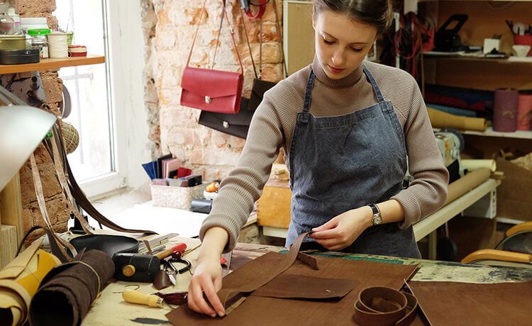 Junge Sattlerin steht in einer Werkstatt und schneidet Lederteile für eine Tasche. Junge Sattlerin steht in einer Werkstatt und schneidet Lederteile für eine Tasche.