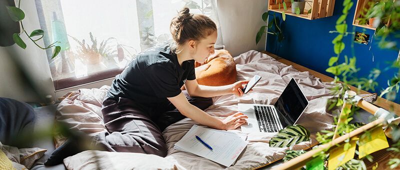 Mädchen sitzt mit Laptop auf dem Bett und informiert sich über Ausbildungsarten.