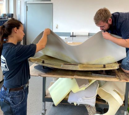 Eine junge Frau und ein junger Mann verkleiden ein Autoteil. Eine junge Frau und ein junger Mann verkleiden ein Autoteil.