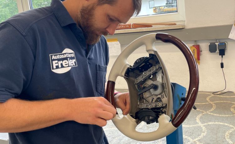 Ein Autosattler arbeitet daran, ein Lenkrad zu verkleiden. Ein Autosattler arbeitet daran, ein Lenkrad zu verkleiden.