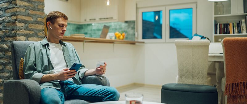 Azubi sitzt auf einem Sessel und informiert sich am Handy über finanzielle Zuschüsse.