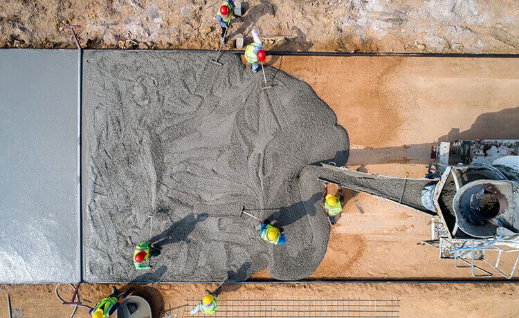 Blick von oben auf eine Baustelle, bei der gerade ein Betonfundament gegossen wird.