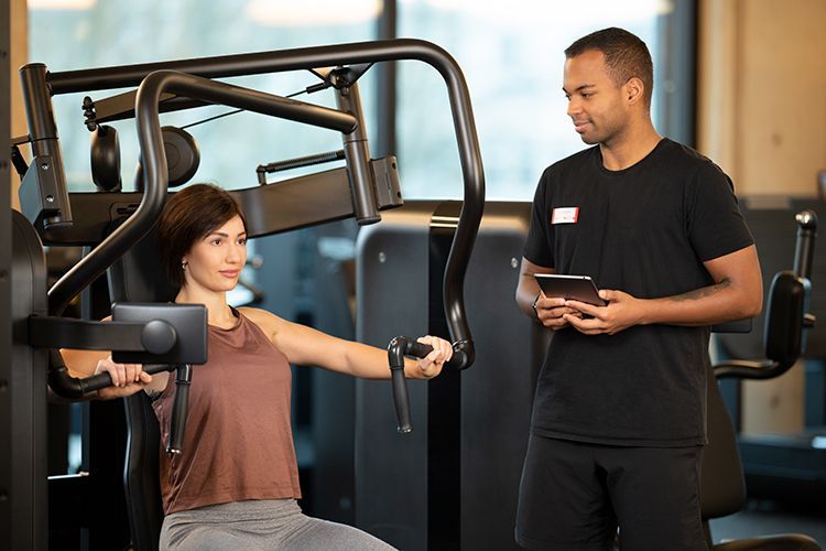 Trainer zeigt einer Frau ein Gerät im Fitnessstudio. 